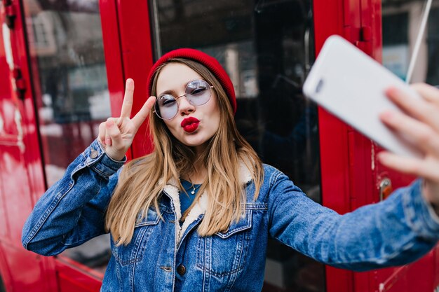 Lovely young woman with red lips making selfie in spring day and using phone.