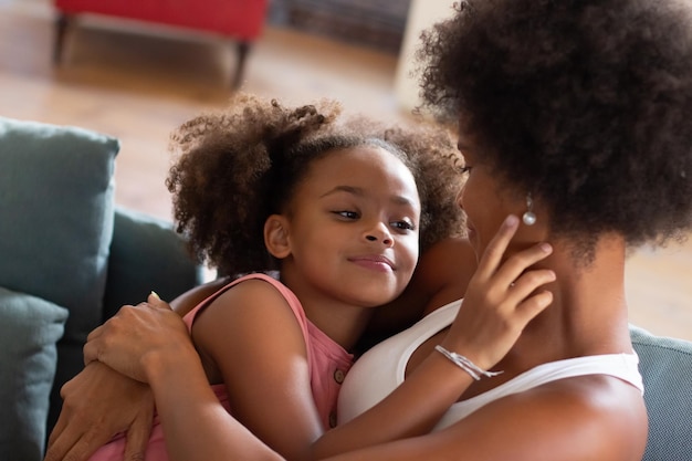 Free photo loving african american mother and daughter hugging. woman and girl in casual clothes holding each other on coach. love, family, bonding concept