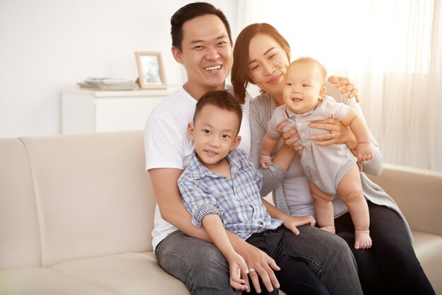 Любящая азиатская пара позирует на диване у себя дома с маленьким сыном и ребенком