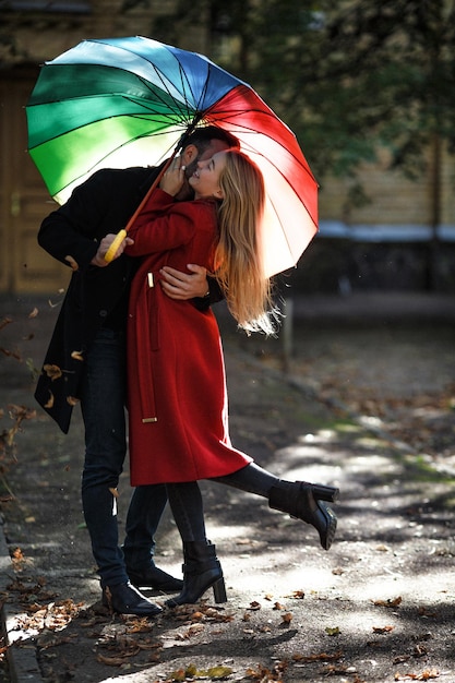 Влюбленная пара в модных пальто, стоя под красочным зонтиком.