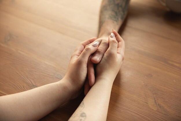 Loving couple holding hands close-up on wooden desk