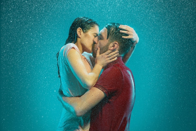 Free photo the loving couple kissing in the rain on a turquoise background