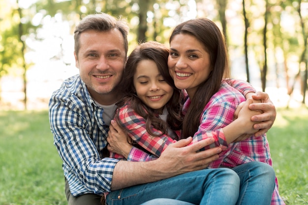 Loving couple looking at camera hugging their daughter in park