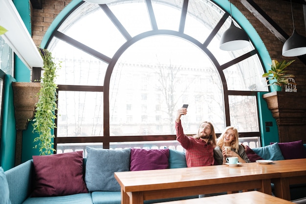 Free photo loving couple sitting in cafe and talking while make selfie.