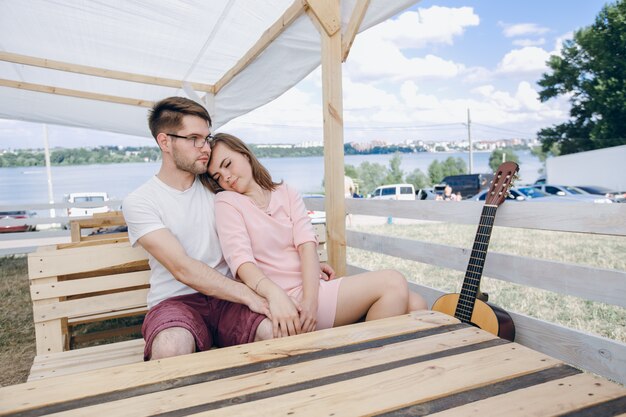 Любить пара сидит на деревянной скамейке с гитарой рядом с ним