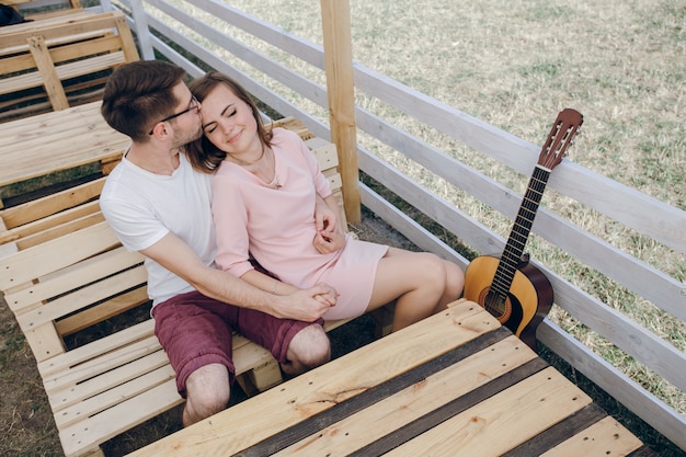 Loving couple sitting on a wooden bench with a guitar next to it