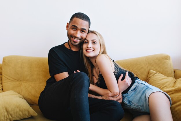 Loving couple smiling, hugging, looking. Lovers in home clothes sitting on couch and cuddle. Coziness, comfort, relaxation.