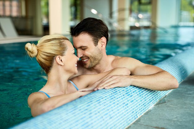 Loving couple talking face to face while being in the water of indoor swimming pool at the spa