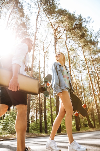 Free photo loving couple walking with skateboards outdoors. looking aside.