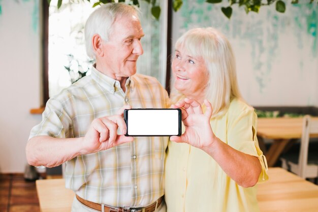 Loving elderly couple showing smartphone to camera