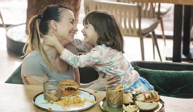 Loving family. Mom with cute daughter eating fast food in a cafe, family and nutrition concept