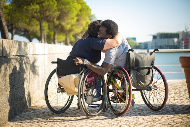 Loving family in wheelchairs spending time near water. African American man and Caucasian woman in casual clothes, hugging. Love, affection, happiness concept