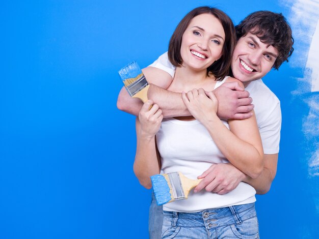 Loving happy couple standing in embrace with paintbrush near the wall