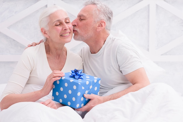 Loving husband kissing his wife on cheek holding blue gift box in hand