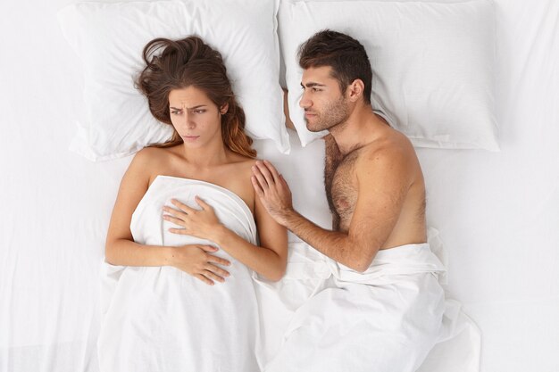 愛する夫は、問題を抱えている妻を支えて落ち着かせ、白い寝具の下で一緒にベッドにとどまり、否定的な感情を表現しようとします。家族の悩み、人間関係、ストレスの多い状況