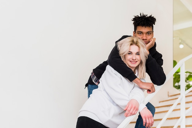 Free photo loving interracial young couple standing on staircase looking at camera