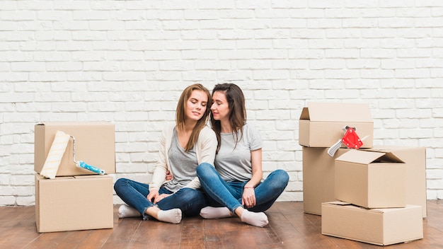 Любящие молодые лесбиянки сидят на деревянном полу с движущимися картонными коробками в своем новом доме