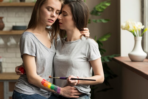 Loving lesbian young couple with paintbrush and painted rainbow flag on hand