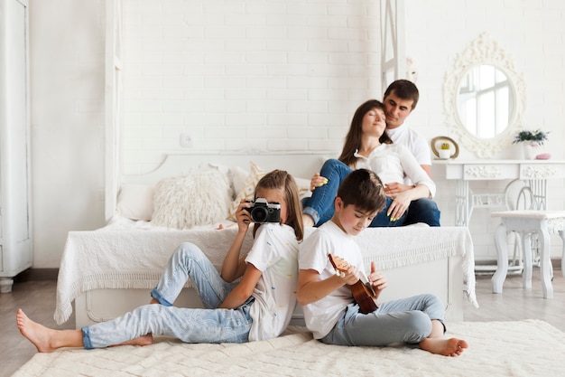 우쿨렐레 연주 카메라와 아들을 들고 침대와 그들의 딸에 앉아 사랑의 부모