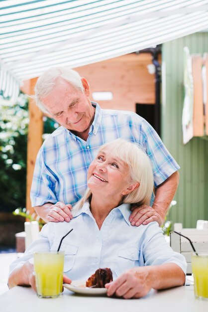 Loving senior couple hugging in cafe on terrace enjoying refreshing drinks