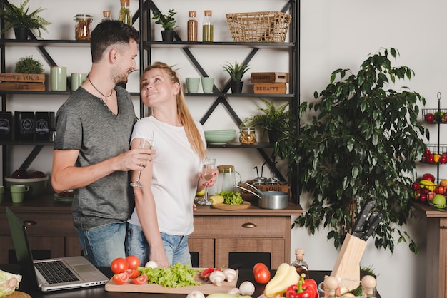 Free photo loving young couple holding champagne flute standing in the kitchen