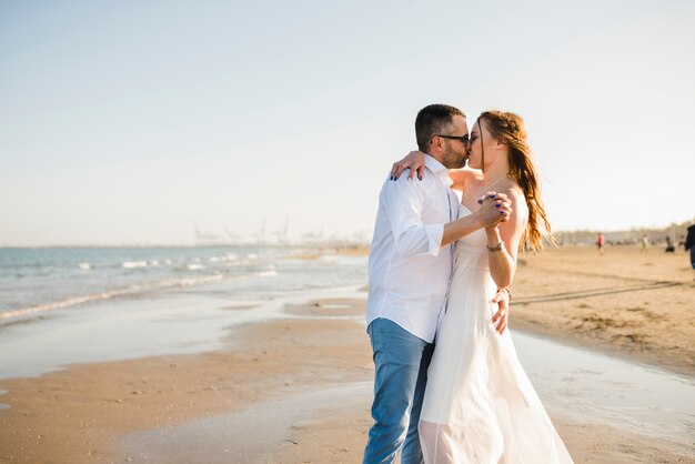 Любящая молодая пара, держа друг друга за руки, целуя друг друга на пляже летом