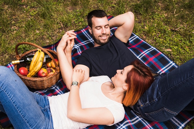ピクニックのバスケットと芝生の上に毛布に横たわる若いカップルを愛する