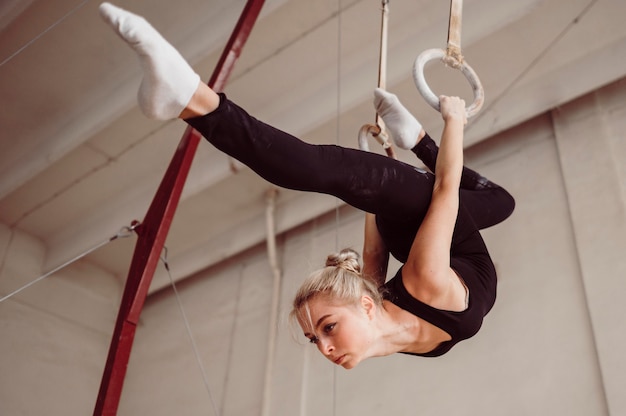 Низкоугольная спортивная женщина тренируется на гимнастических кольцах