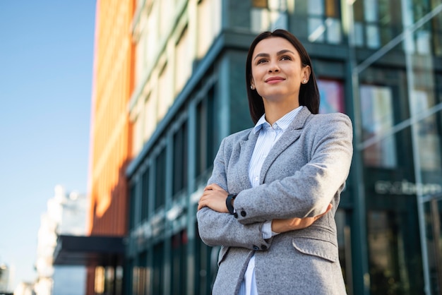 Free photo low angle of businesswoman posing with arms crossed outdoors