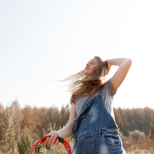 Low angle of of carefree woman in nature holding tambourine