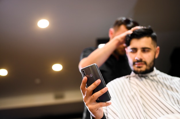 Free photo low angle costumer at barber shop looking at phone with copy space