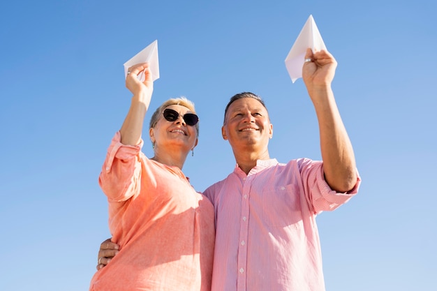 Бесплатное фото Пара под низким углом, держащая бумажные самолетики