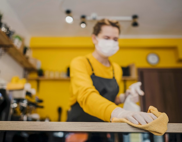 Low angle of female barista cleaning with medical mask on