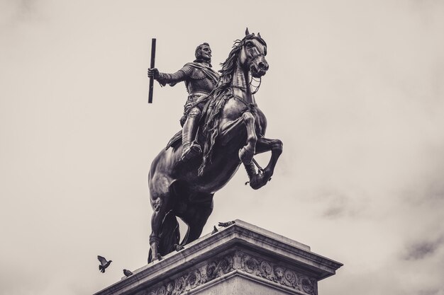 Low angle grayscale shot of a statue in front of the Royal Palace of Madrid