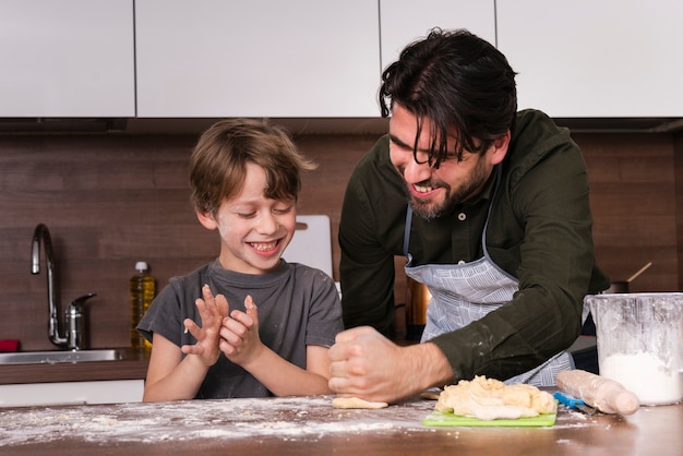 Free photo low angle little boy with father rolling dough