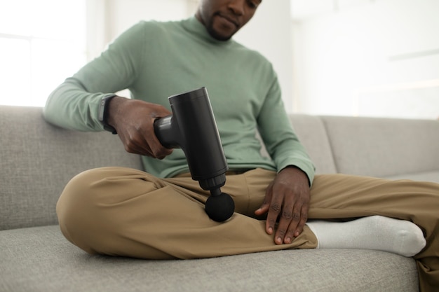 Low angle man using massage gun for leg pain