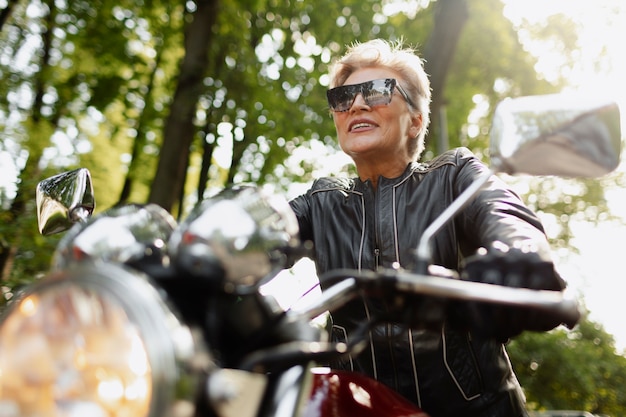 Foto gratuita vecchia donna ad angolo basso con una bella motocicletta