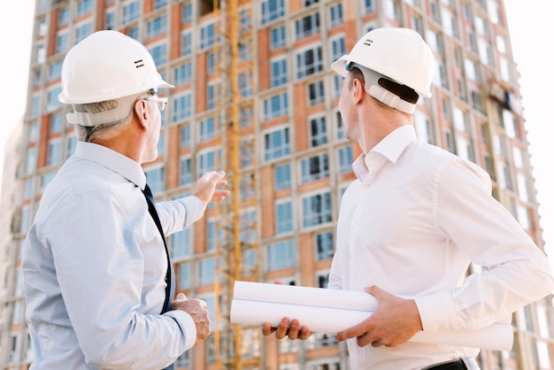 Free photo low angle people with helmets looking at scaffolding design