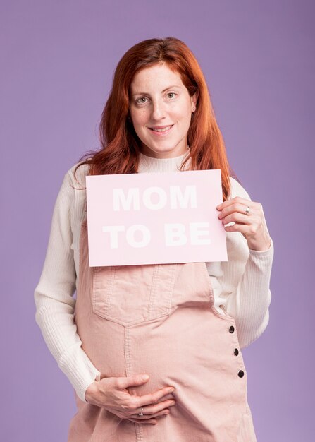 Low angle pregnant female holding paper with mom to be message