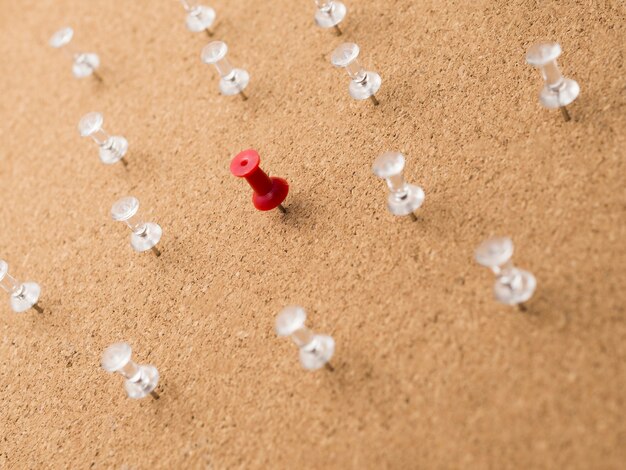 Low angle red pin surrounded by white pins on wooden board