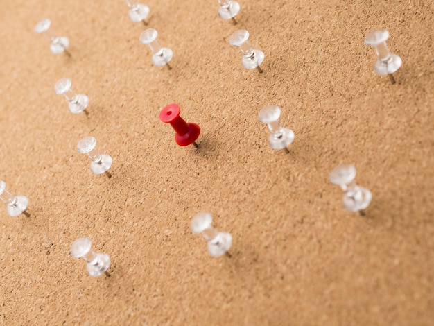 Low angle red pin surrounded by white pins on wooden board