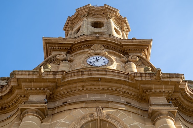 Free photo low angle shot of a catholic church with a clock under a blue sky