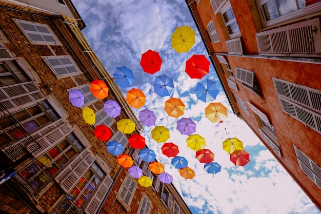 Foto gratuita colpo di angolo basso degli ombrelli variopinti che appendono in mezzo alle costruzioni con il cielo nuvoloso