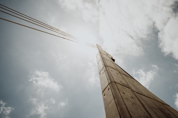 Low angle shot of a concrete column with cables against a bright cloudy sky