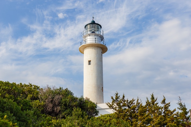 Low angle shot of a lighthouse with cloudy blue sky seen through trees
