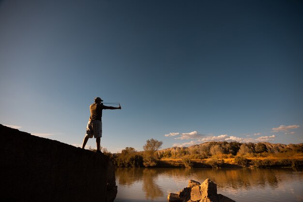 Low angle shot of a male playing with a slingshot at sunset