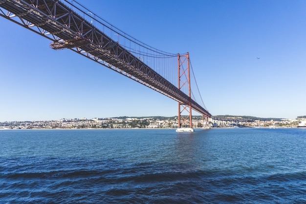 Low angle shot of a Ponte 25 de Abril bridge over the water with the  city in the distance