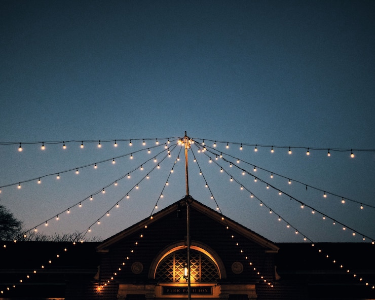 Free Photo low angle shot of strings of light bulbs attached to a pole in front  of a park pavilion at dusk