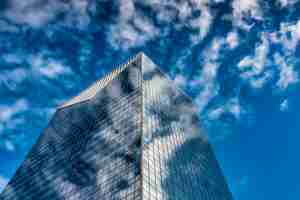 Foto gratuita inquadratura dal basso di un edificio di vetro alto sotto un cielo nuvoloso blu