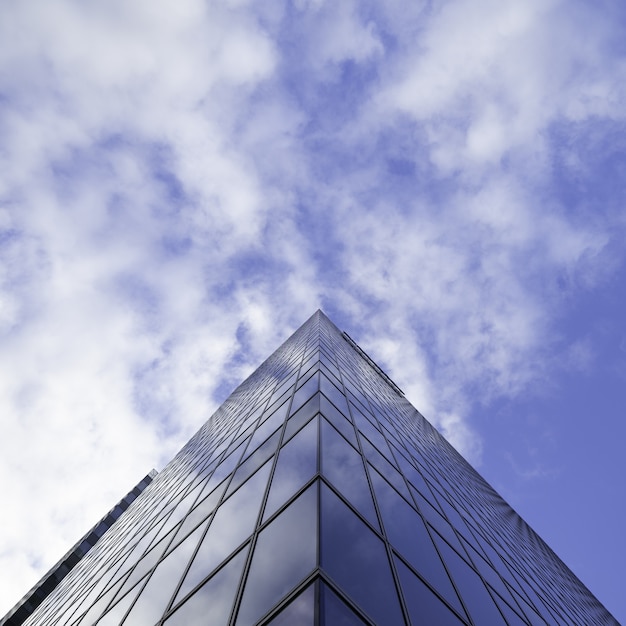 Low angle shot of a tall glass skyscraper business building with cloudy sky